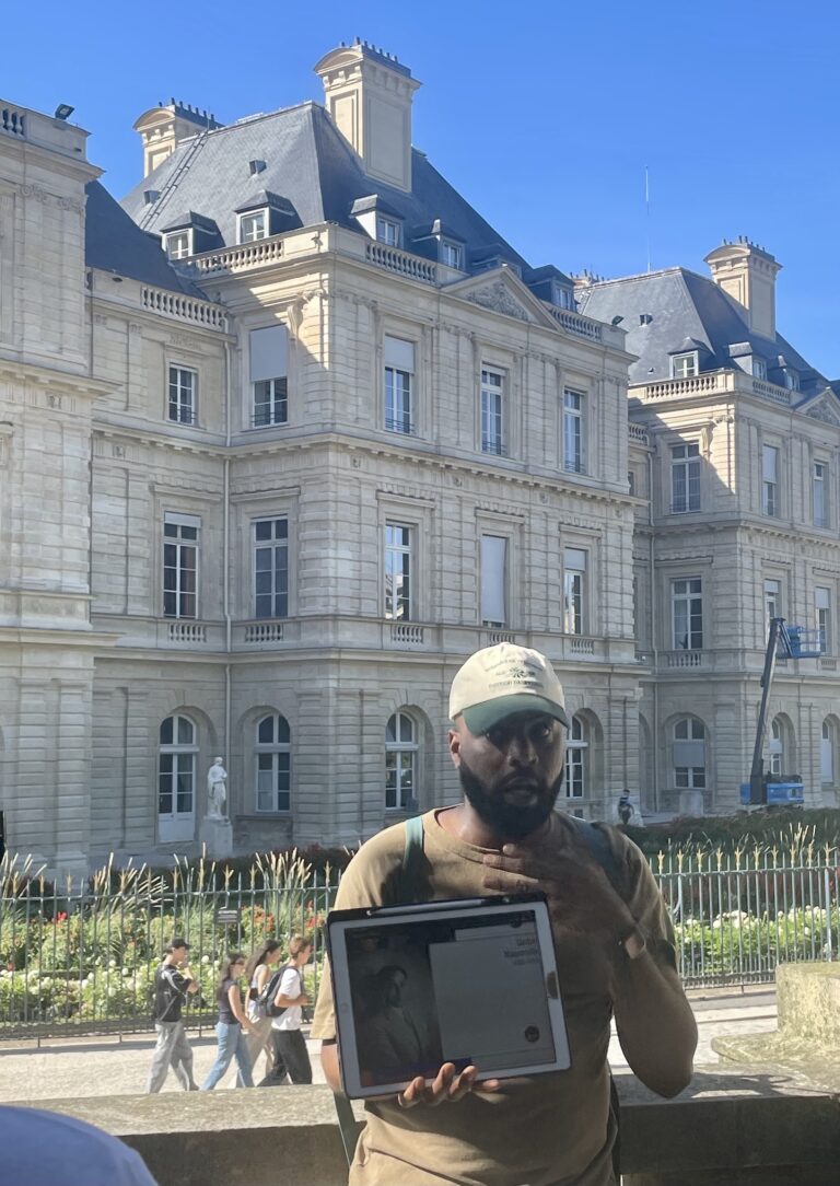 Kévi Donat devant le palais du Luxembourg, siège du Sénat, nous montrant une photo de Gaston Monnerville © Soraya Patel De Zorzi